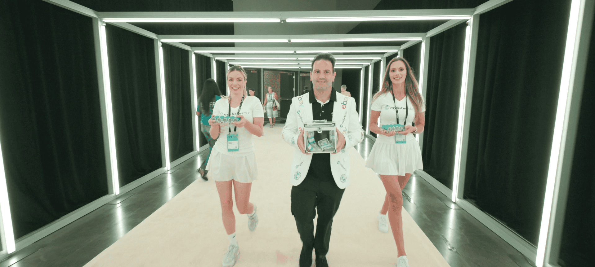 MyListerHub team walking through the eBay Open 2025 welcome tunnel carrying the $1,000 cash raffle prize box and casino-chip giveaways